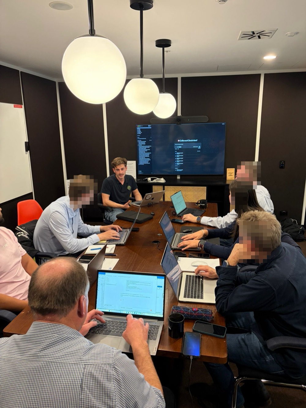Adam running a client workshop around a boardroom table, Claude on the screen